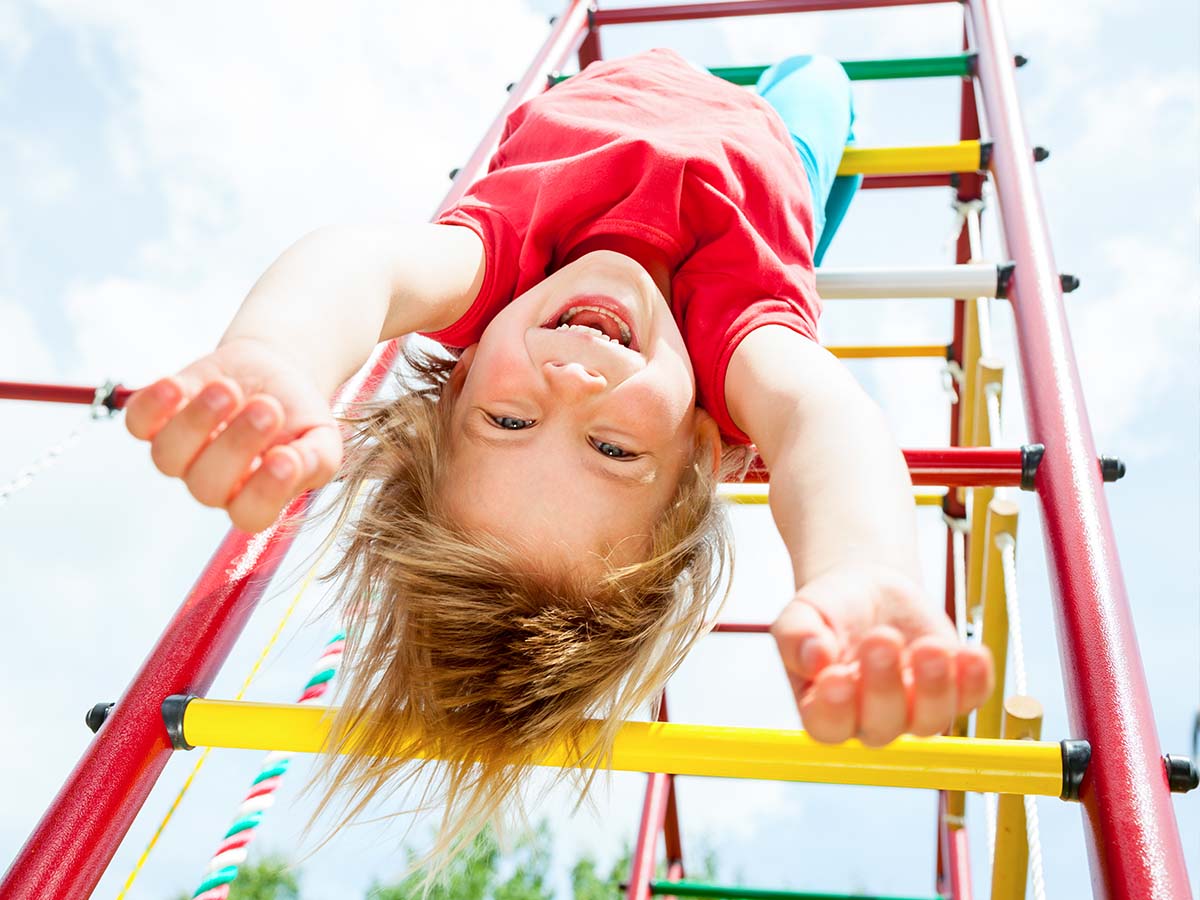Mädchen hängt kopfüber an Klettergerüst auf Spielplatz