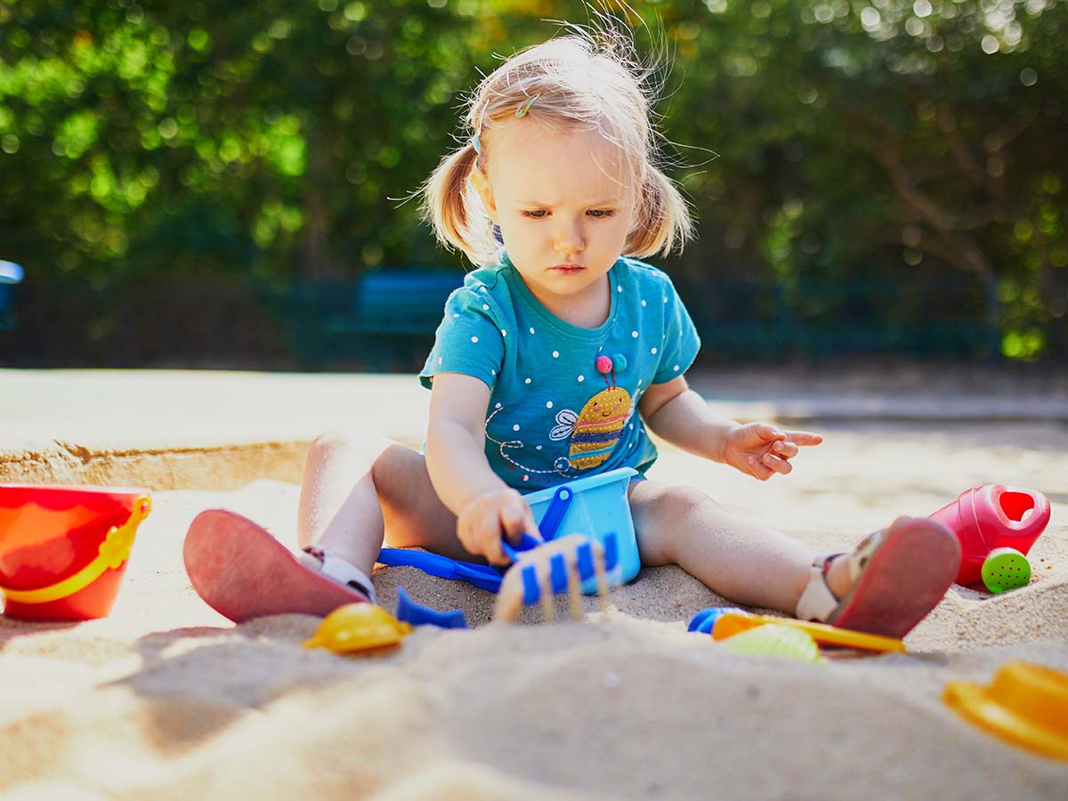 Kleines Mädchen spielt in Sandkasten auf Kinder-Spielplatz