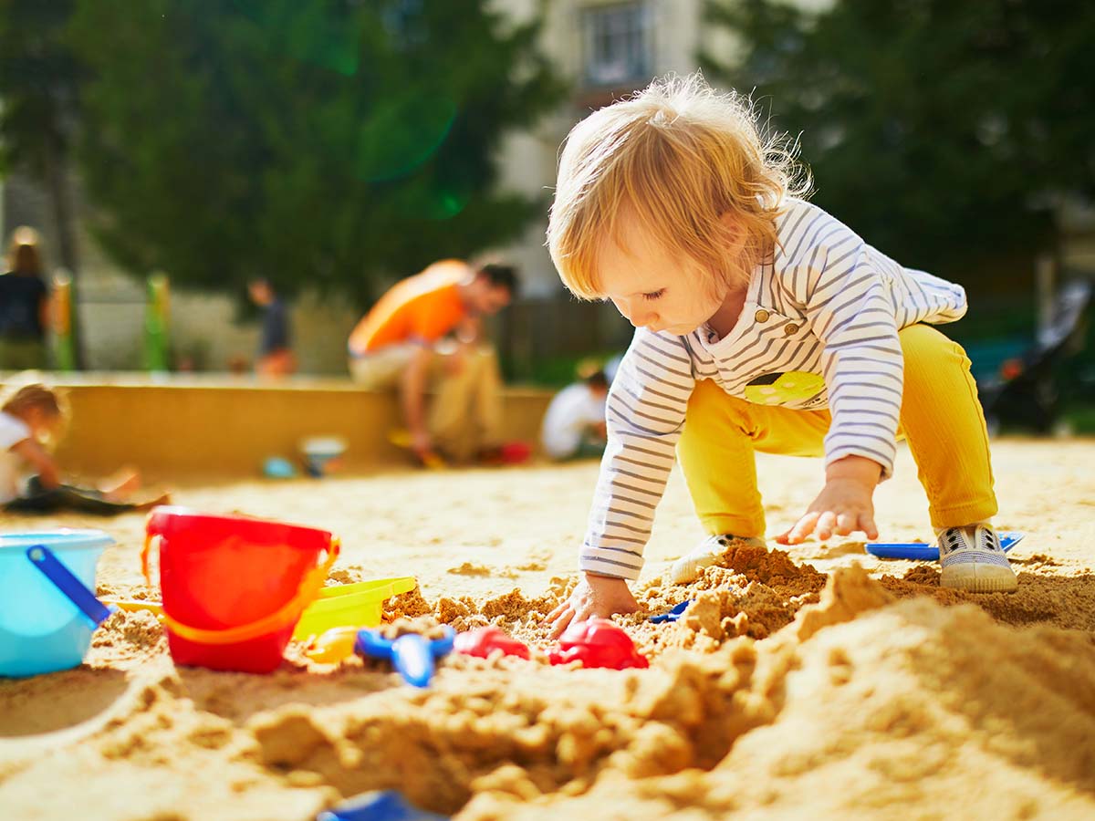 Kleines Mädchen spielt in Sandkasten von Kinder-Spielplatz