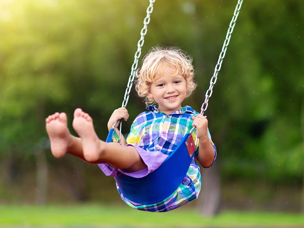 Kleiner Junge schaukelt fröhlich auf Kinder-Spielplatz