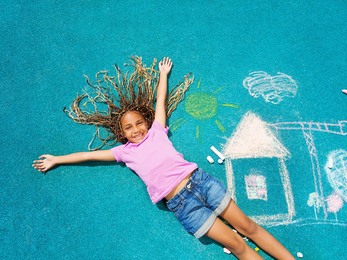 Mädchen liegt auf buntem Fallschutzboden auf Kinder-Spielplatz