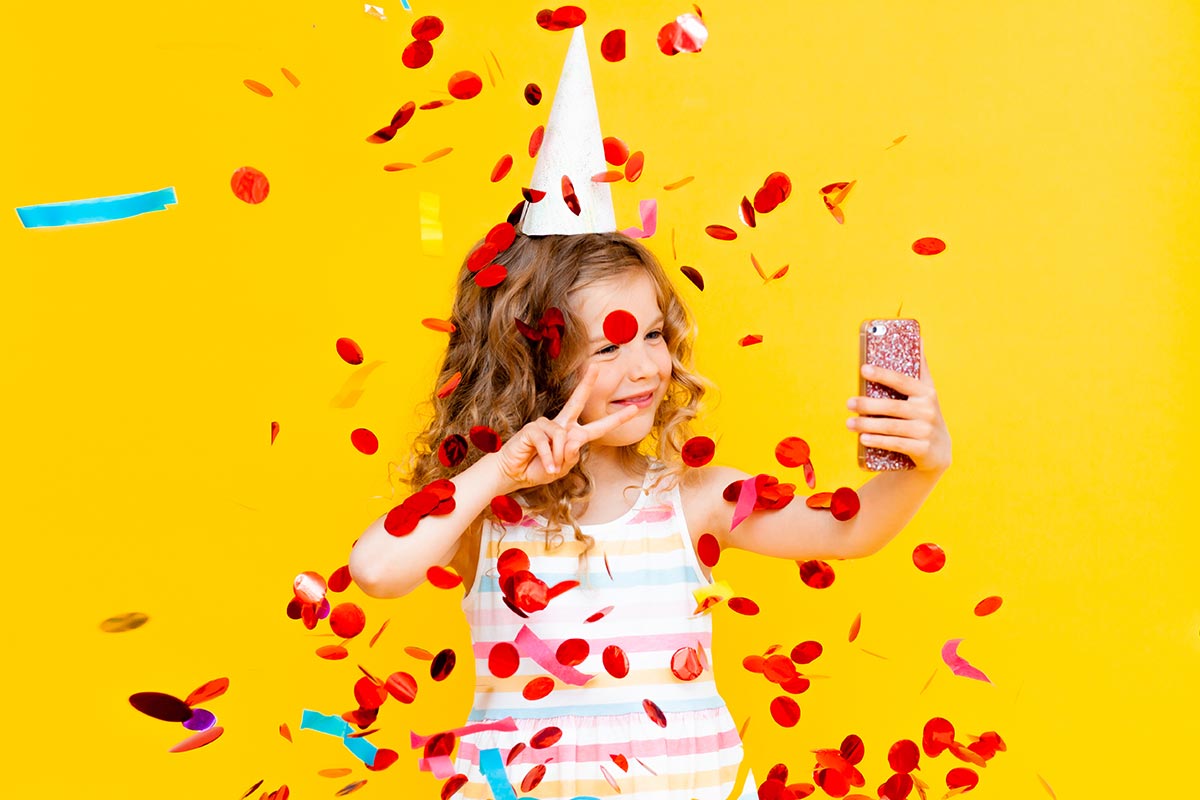 Mädchen macht Selfie mit Konfetti und Partyhut zum Jubeltag