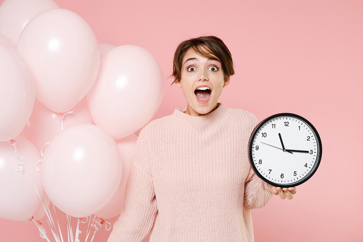 Junge Frau hält Uhr und Ballons zu nachträgliche Geburtstagswünschen