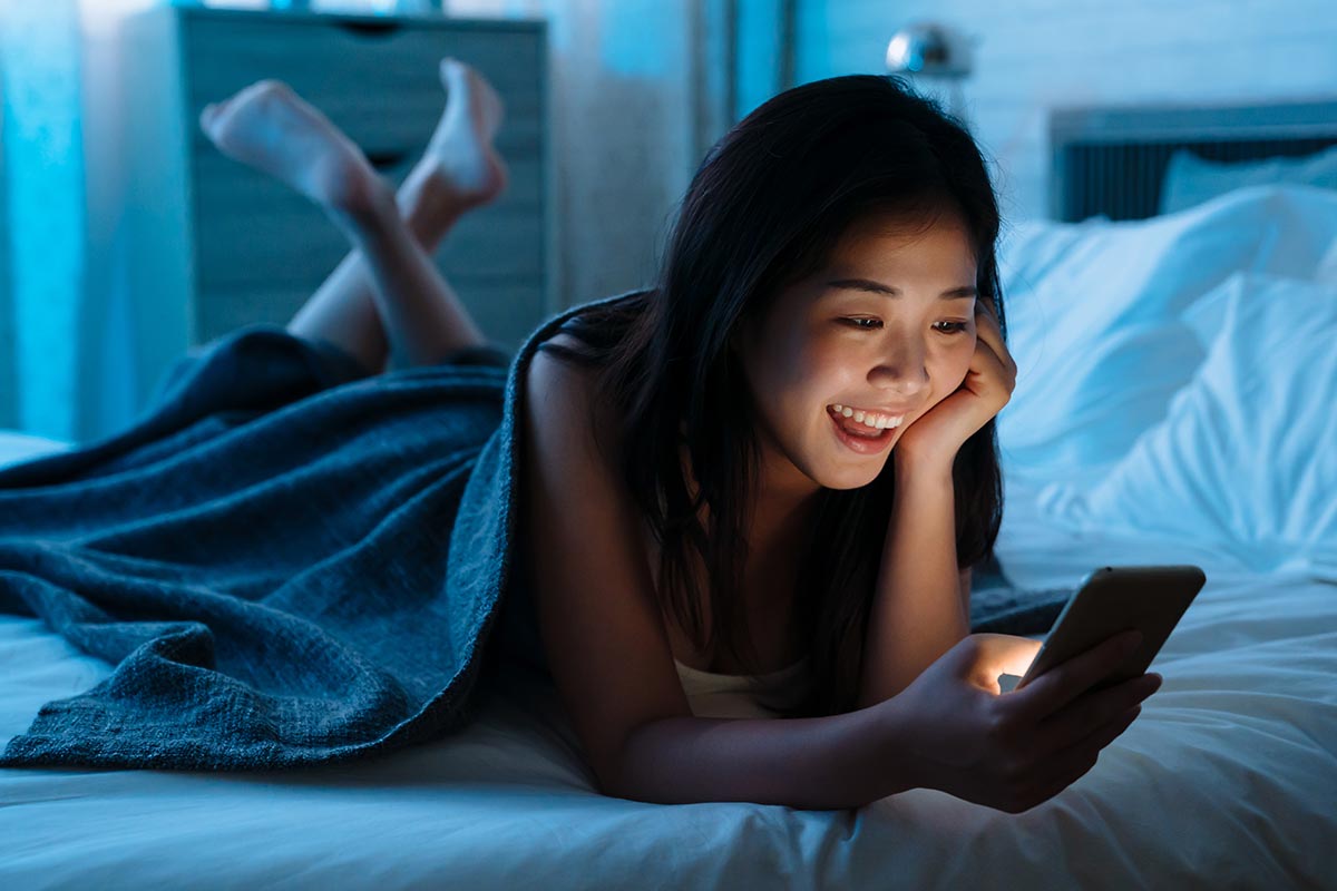 Junge Frau lacht über lustige Gute-Nacht-Sprüche auf Handy