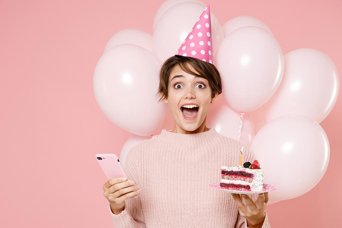 Junge Frau freut sich über witzige WhatsApp-Geburtstagswünsche mit Torte und Ballon