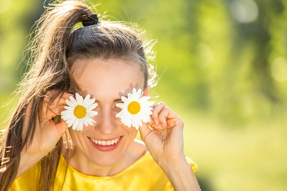 Frau hält Blüten vor Augen und lacht über lustige Sprüche
