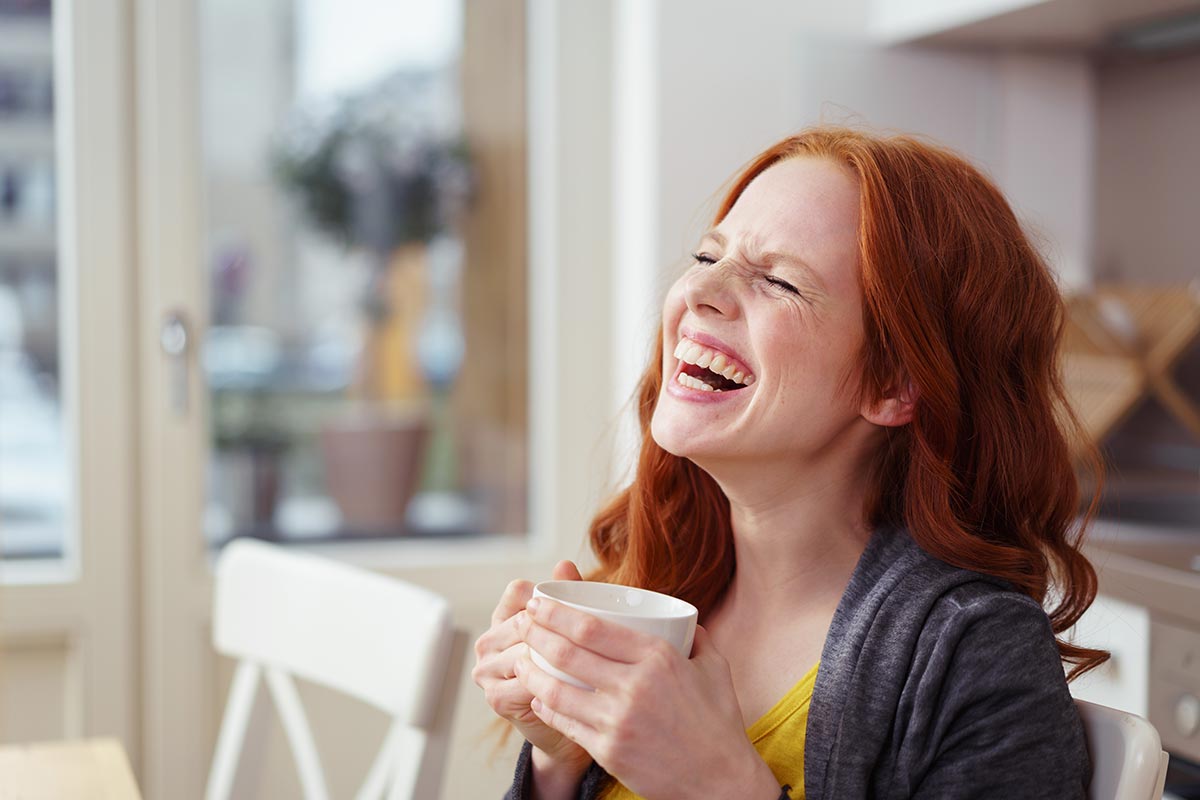 Junge Frau lacht über lustige Guten-Morgen-Sprüche am Morgen