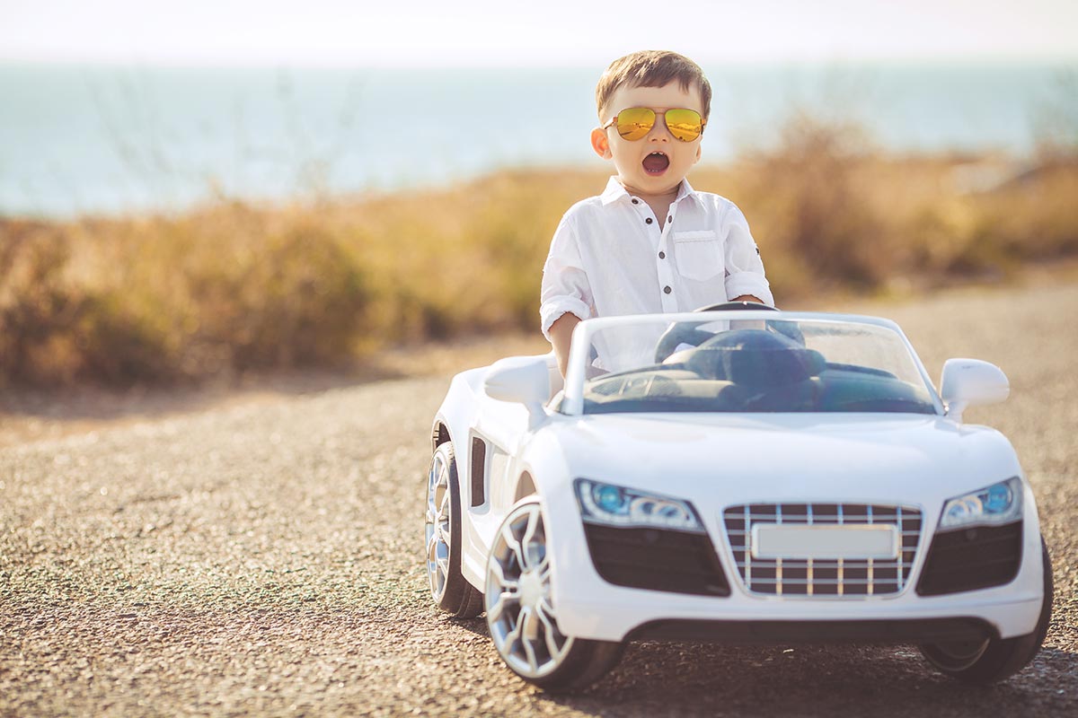 Kleiner cooler Junge sitzt in coolem Kinder-Auto