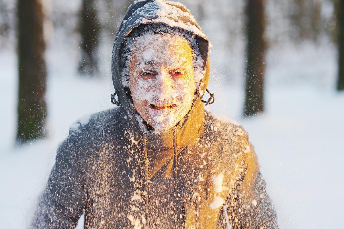 Junger Mann mit Schnee im Gesicht lacht über lustige Winter-Sprüche