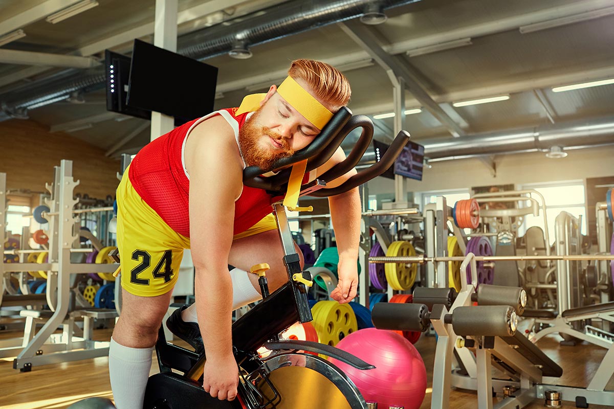 Unsportlicher Mann schläft auf Fahrrad in Fitnessstudio