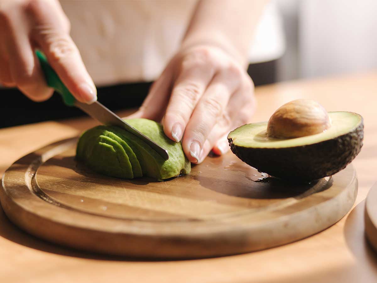 Frau schneidet Avocado auf Holzbrett