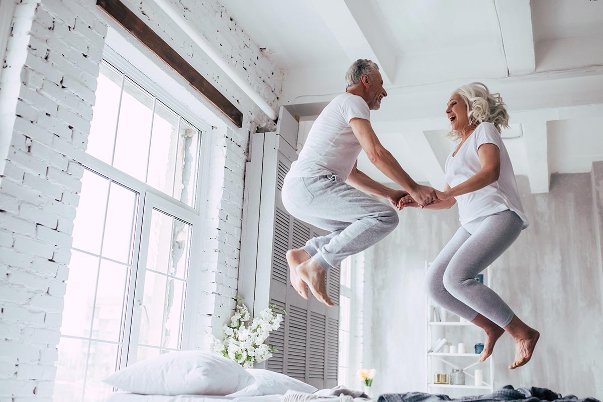 Älteres Paar springt auf Bett und freut sich über lustige Liebessprüche