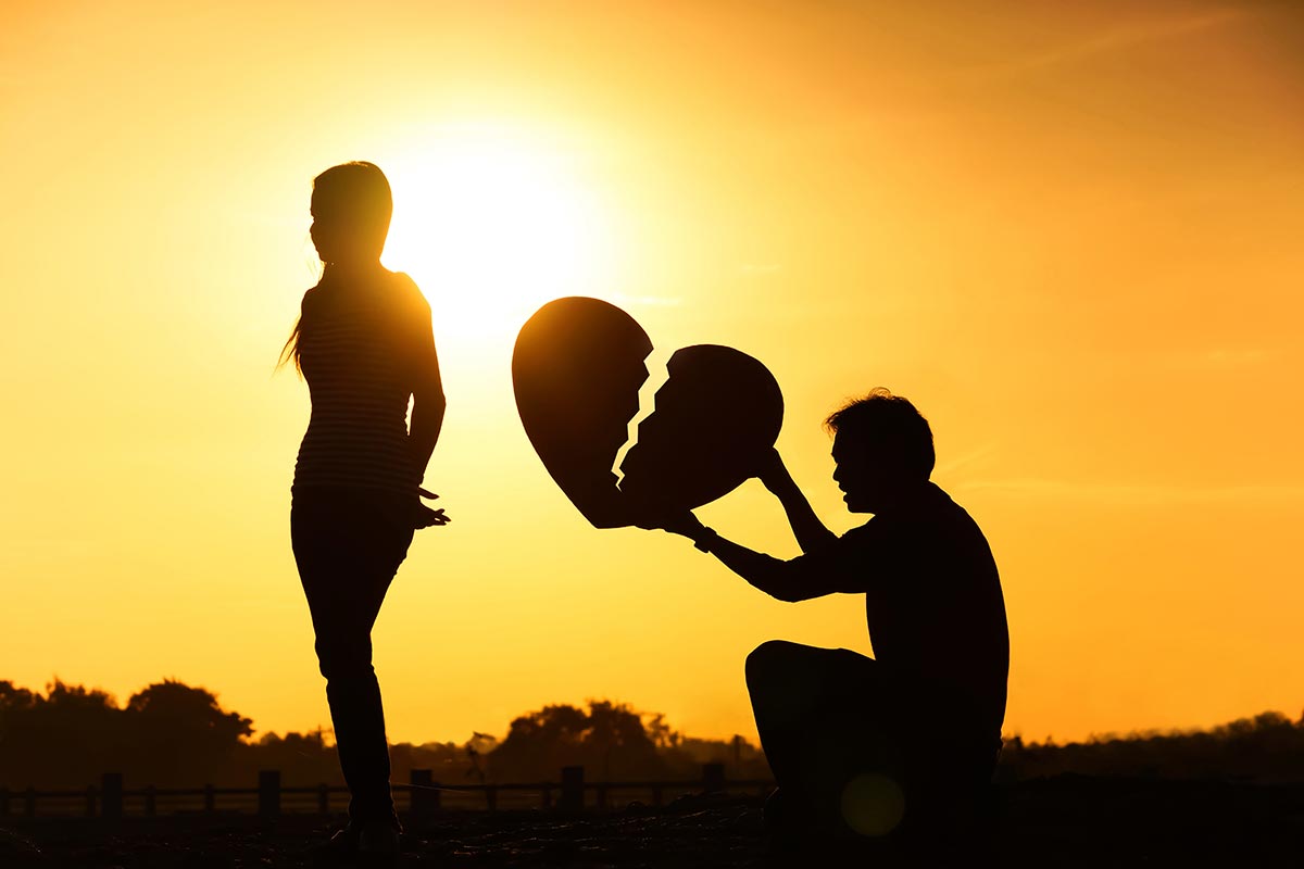 Mann hält hinter Frau zerbrochenes Herz im Sonnenuntergang