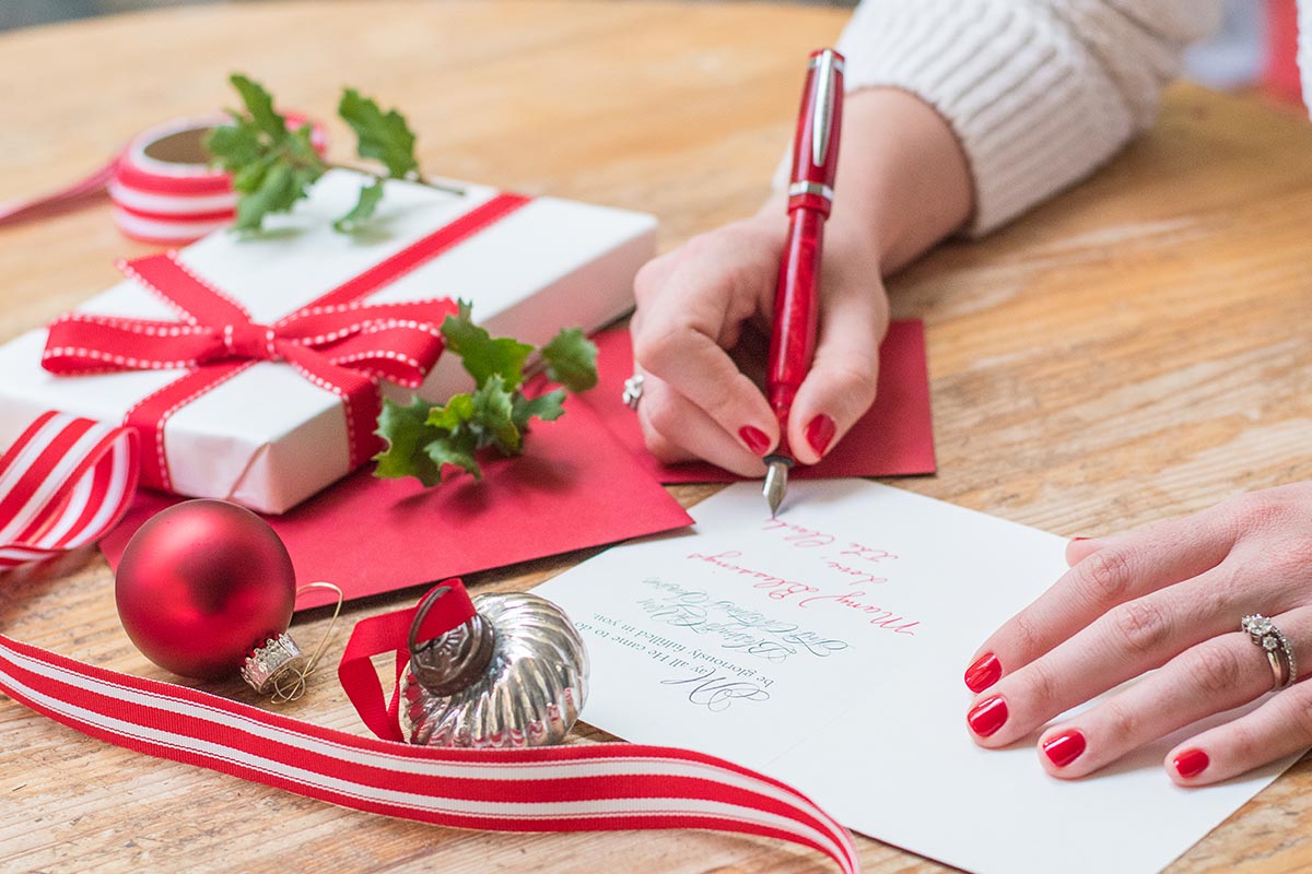 Frau schreibt schöne Weihnachtsgrüße in Karte auf Tisch